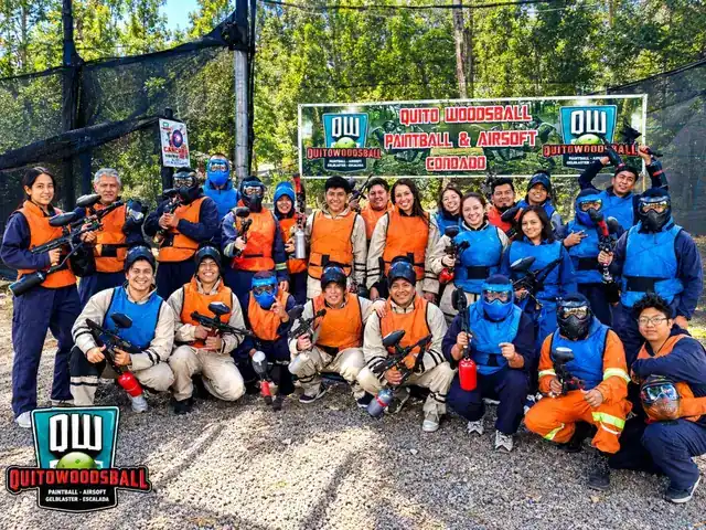 Grupo de jugadores con overoles, chalecos, máscaras y marcadoras de paintball frente al letrero de Quito Woodsball Paintball & Airsoft Condado