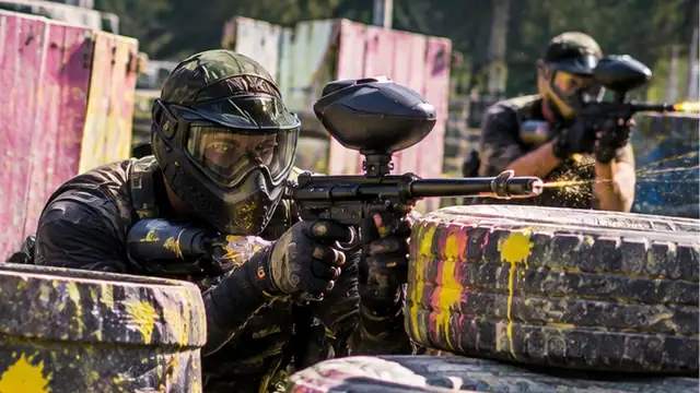 Jugador de paintball con máscara y marcadora disparando detrás de llantas en el campo de Quito Woodsball